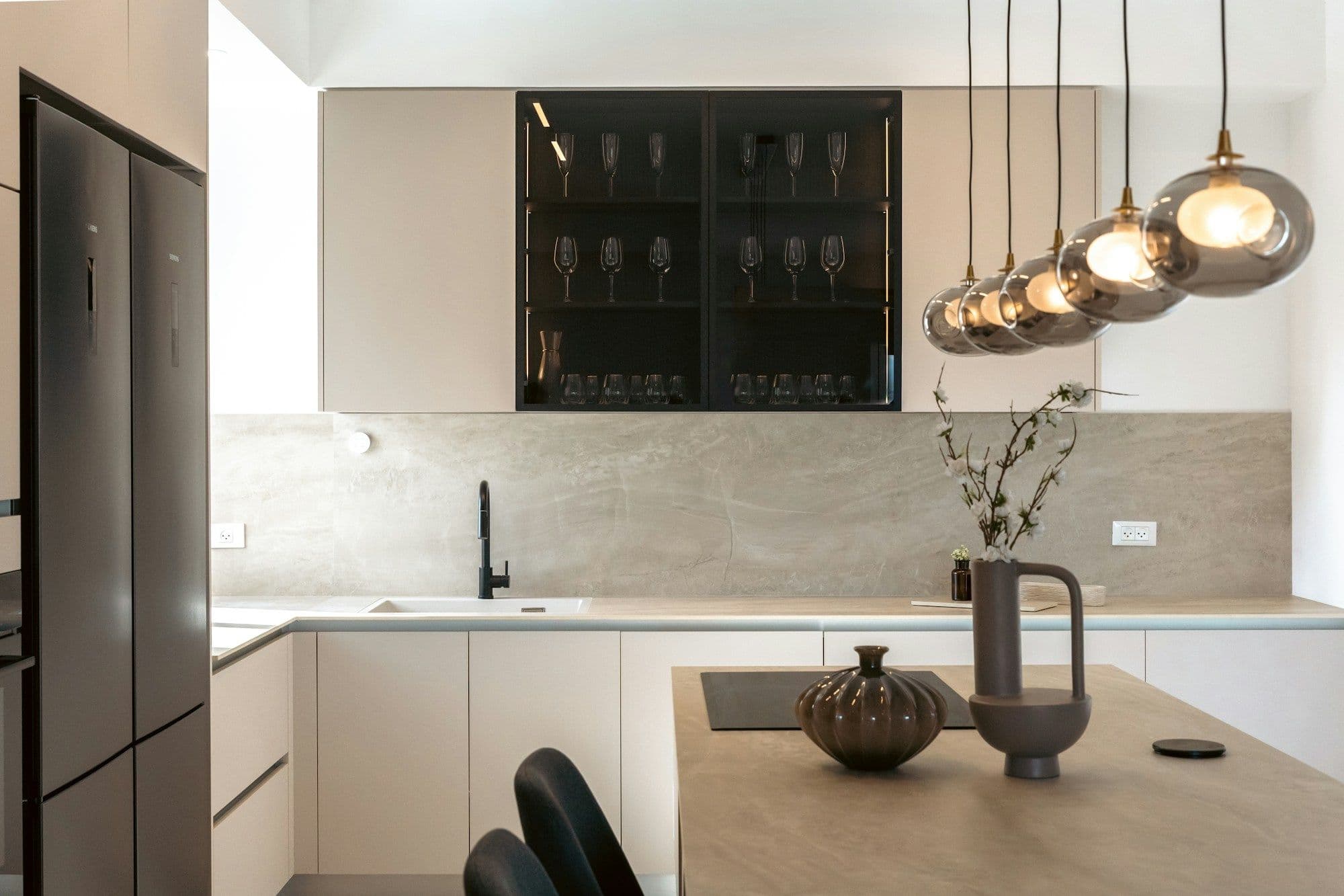 Moderne lichte keuken met een hoge rvs-koelkast, een kookeiland en hanglampen.